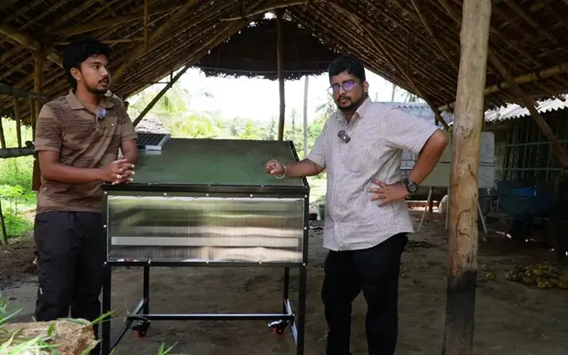 The solar dryer under the thatched work shed, with two of the team beside it